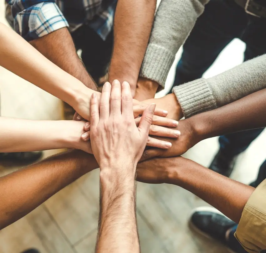 A diverse mix of people all placing their hands on top of each others