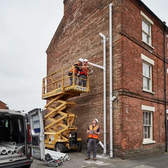 Workers installing soil pipes from a MEWP